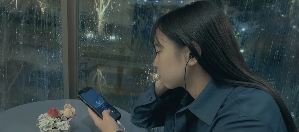 雨の窓辺でスマートフォンを見る女性